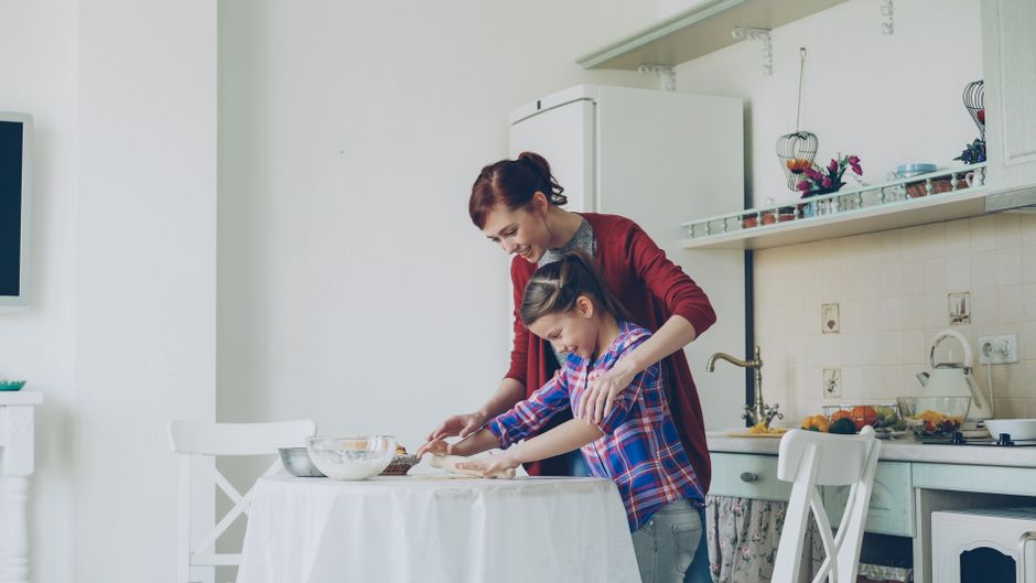 A parent and child rolling out dough together in a bright kitchen