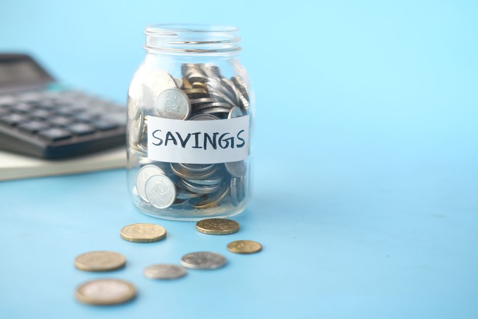 A glass savings jar full of coins next to a calculator